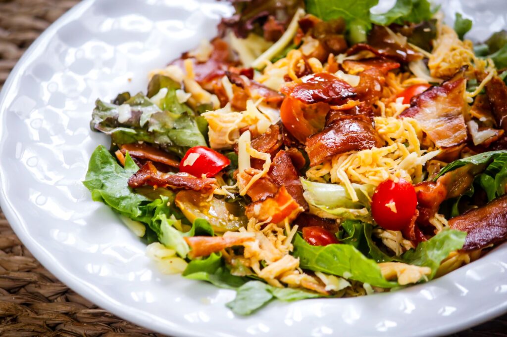 Une salade vibrante avec du bacon croustillant, de la laitue, des tomates cerises et du fromage sur une assiette blanche.