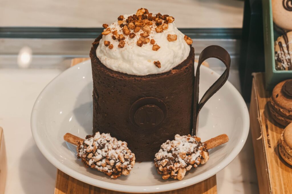 Un gâteau au chocolat en tasse à se lécher les babines, garni de crème fouettée et de noix, servi avec deux sucettes au caramel.