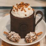 Un gâteau au chocolat en tasse à se lécher les babines, garni de crème fouettée et de noix, servi avec deux sucettes au caramel.