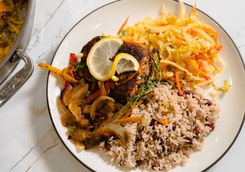 Poisson escovitch jamaïcain tendre servi avec du riz et des pois, accompagné d'une salade de chou colorée sur une assiette.