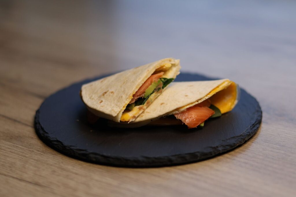 Une tortilla au saumon frais, garnie d'épinards et de fromage, servie sur une ardoise, idéale pour un repas sain.