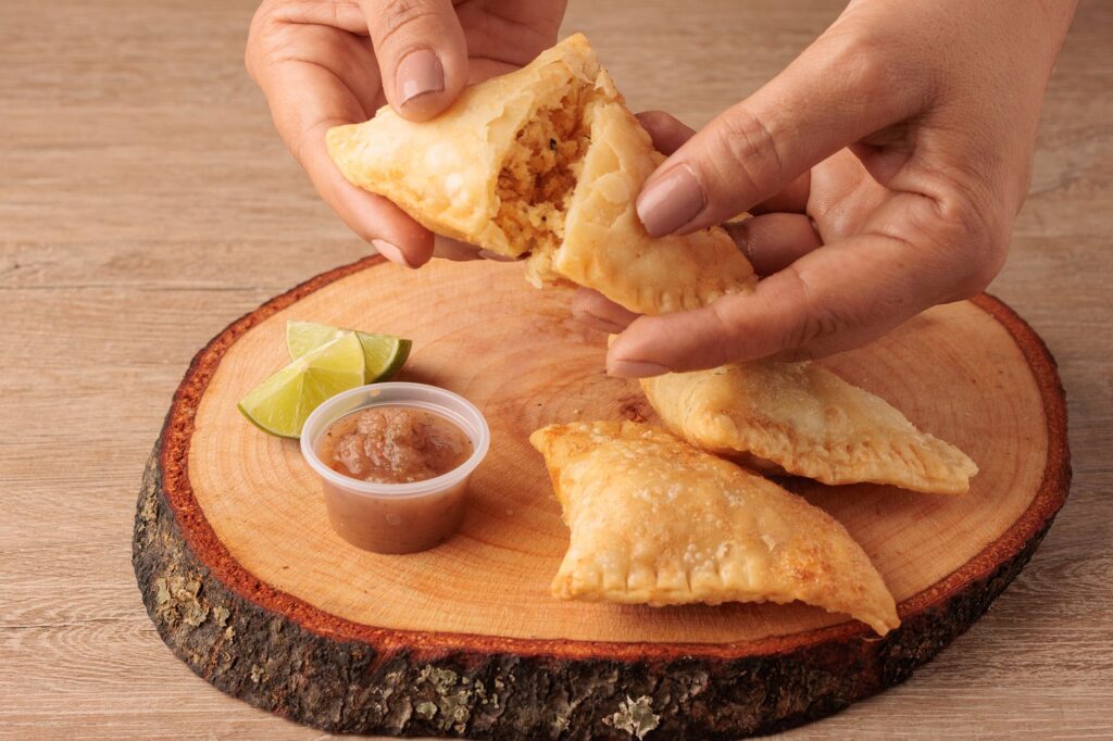 Empanadas colombiennes avec une salsa acidulée et des tranches de citron vert, servies sur un plateau en bois.