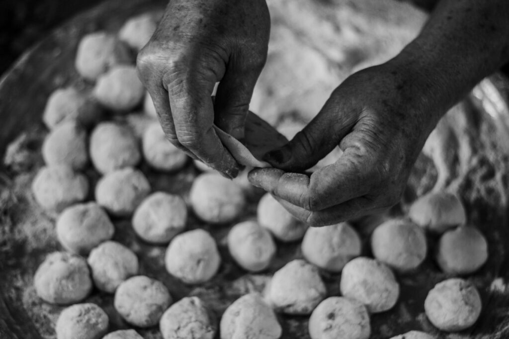 Image en noir et blanc montrant des mains formant des boulettes de pâte sur un plateau, évoquant la cuisine traditionnelle.