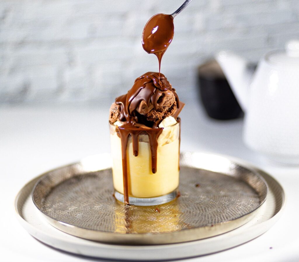Délicieuse coupe glacée au chocolat nappée de sauce, servie dans un verre sur un plateau.