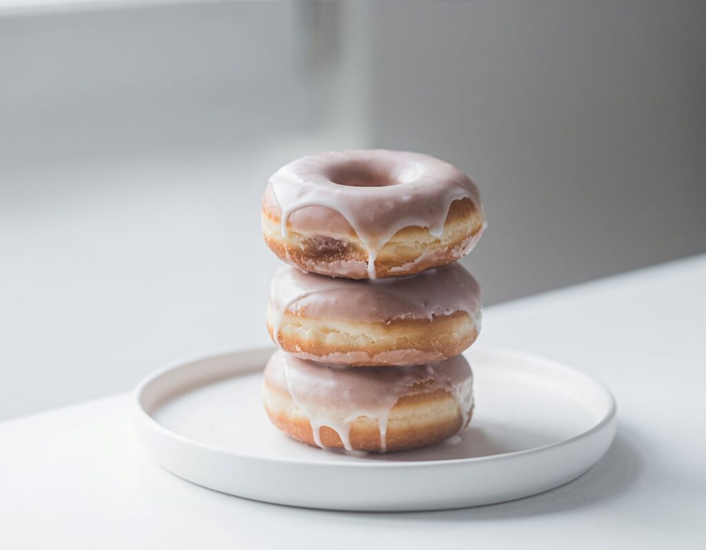 Un gros plan de trois beignets glacés empilés sur une assiette blanche à l'intérieur.