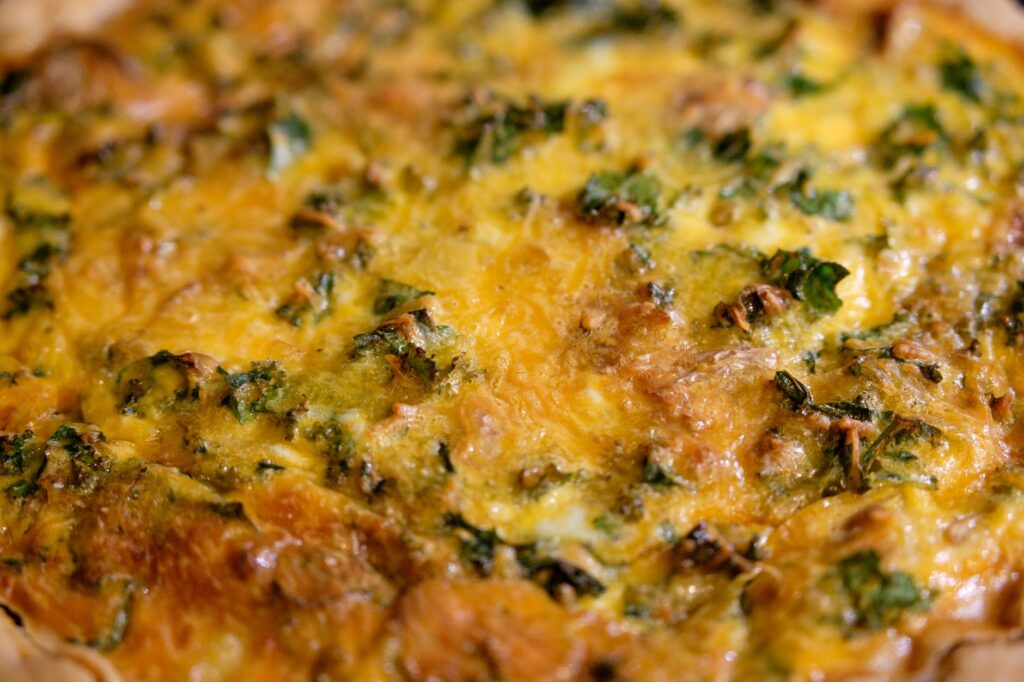 Gros plan sur une quiche dorée et fromagée au chou frisé, parfaite pour le petit-déjeuner ou le brunch.