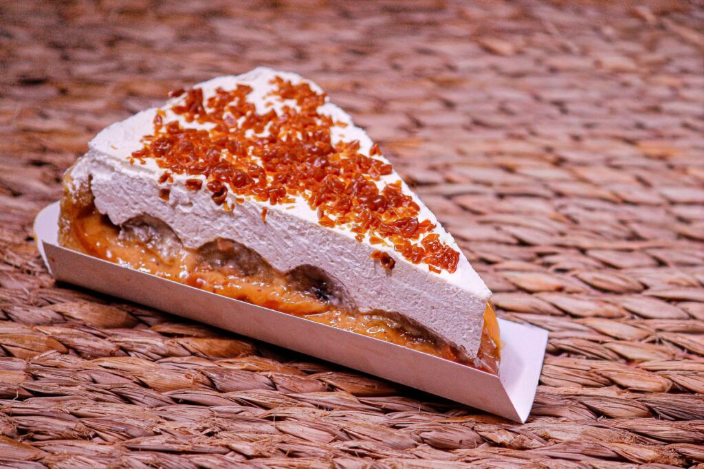 Une part alléchante de tarte banoffee garnie de crème et de caramel, posée sur un tapis en osier.