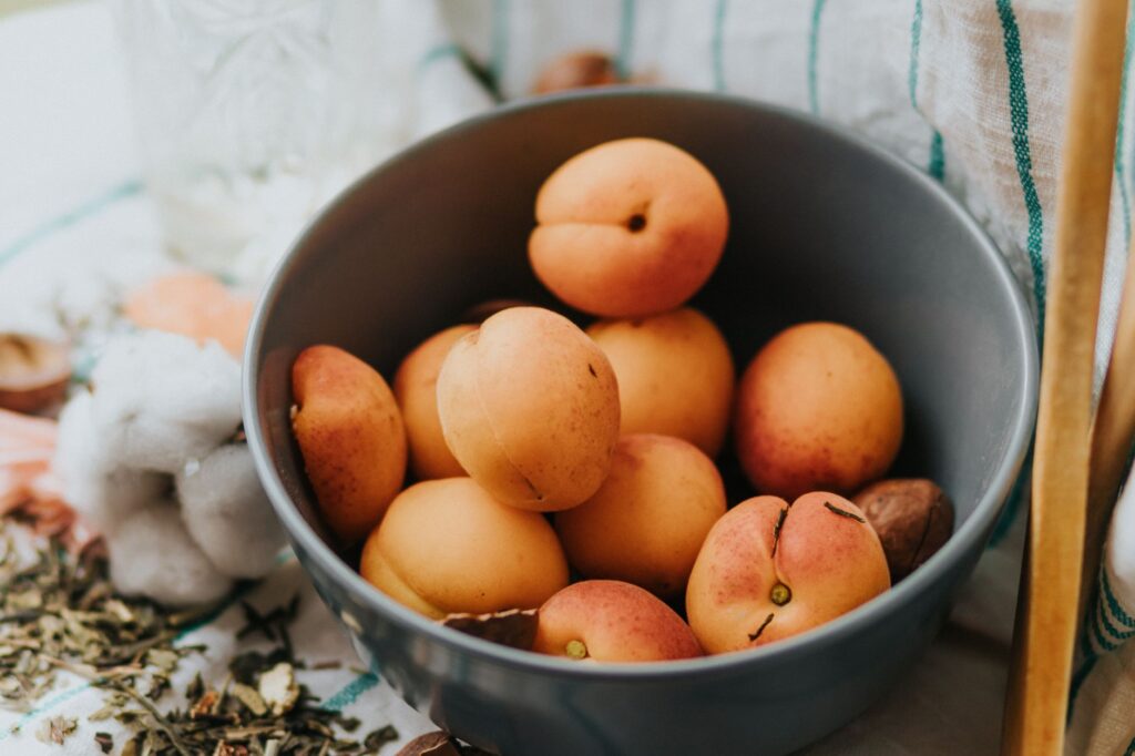 Gros plan sur des abricots frais dans un bol gris, posé sur une table de cuisine et entouré d'herbes aromatiques.