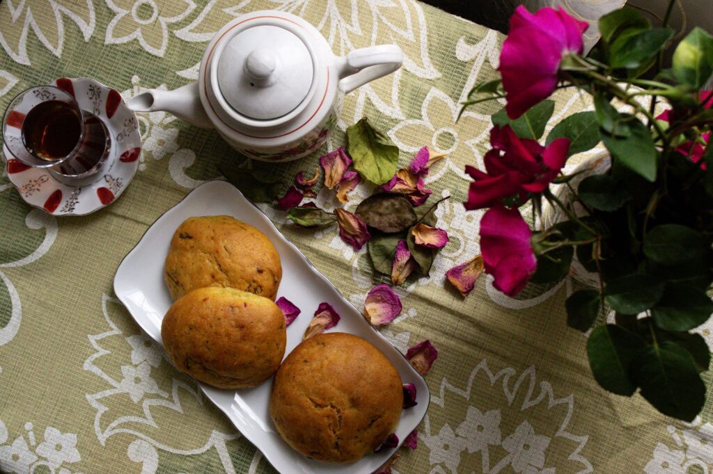 Un service à thé accueillant, avec des petits pains et des roses sur une nappe à fleurs, pour un après-midi chaleureux.