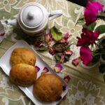 Un service à thé accueillant, avec des petits pains et des roses sur une nappe à fleurs, pour un après-midi chaleureux.