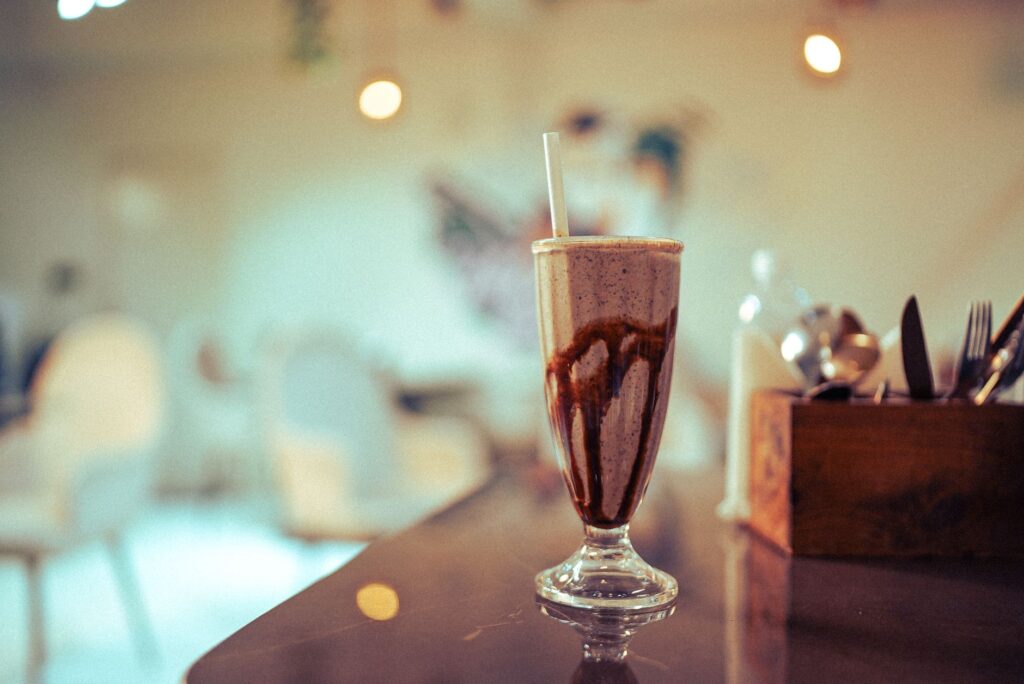 Laissez-vous tenter par un onctueux milkshake au chocolat servi dans un verre élégant, dans le cadre chaleureux d'un café.