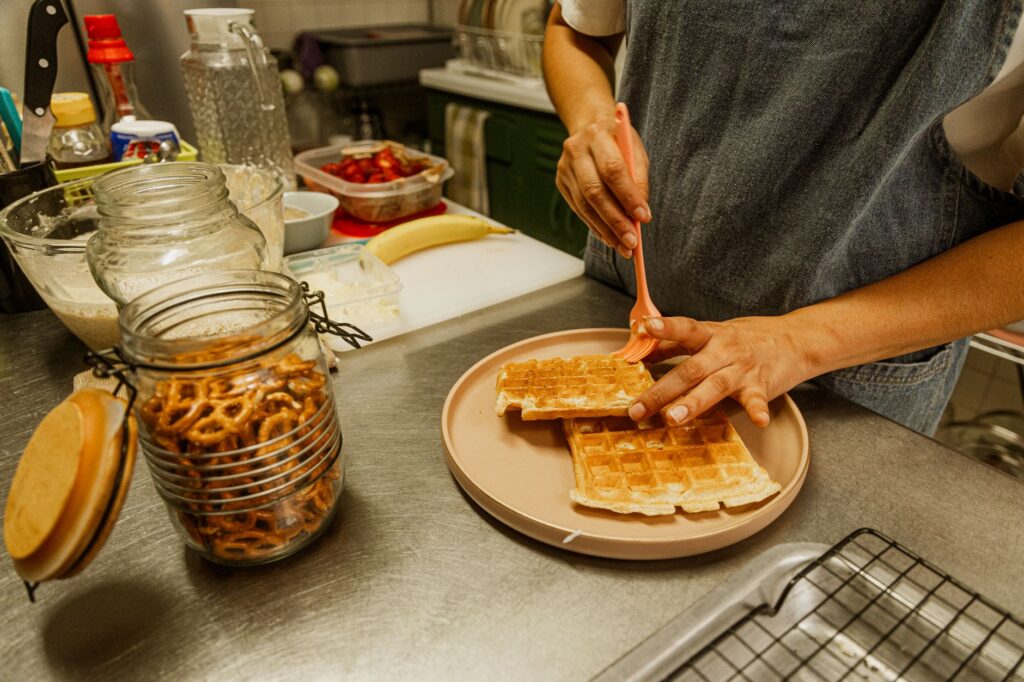 Gros plan sur une personne préparant des gaufres dans une cuisine domestique avec des bretzels et d'autres ingrédients.