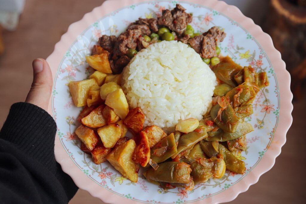 Gros plan sur une assiette composée de riz blanc, de pommes de terre rôties, de haricots verts sautés et de bœuf tendre, offrant un délicieux repas.