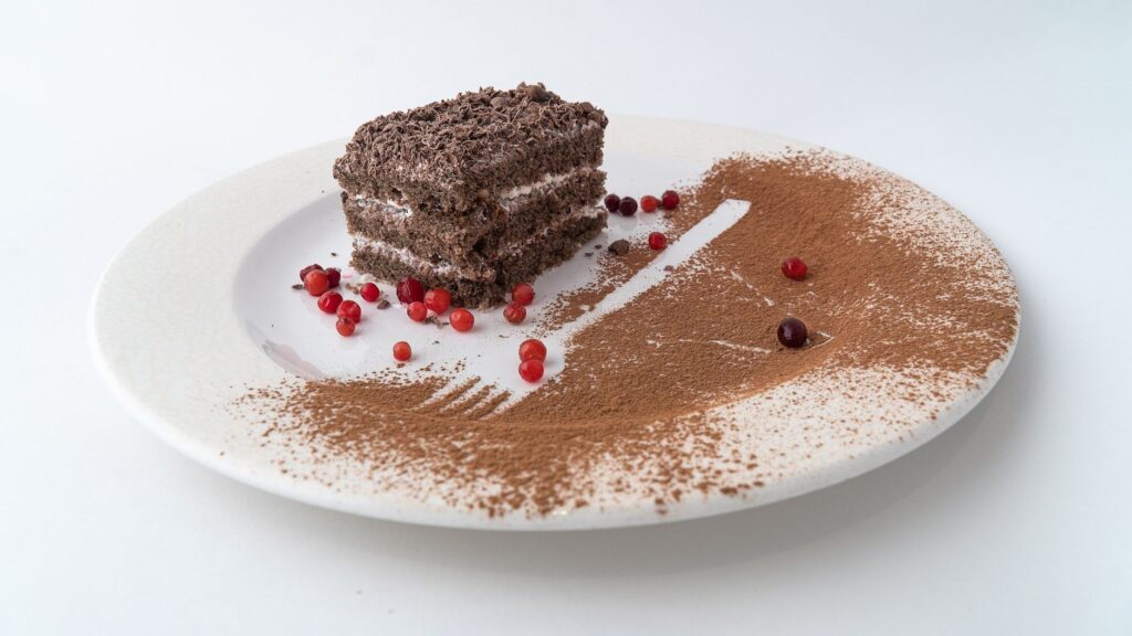 Une délicieuse part de gâteau au chocolat avec des baies et une poudre de cacao sur une assiette blanche.