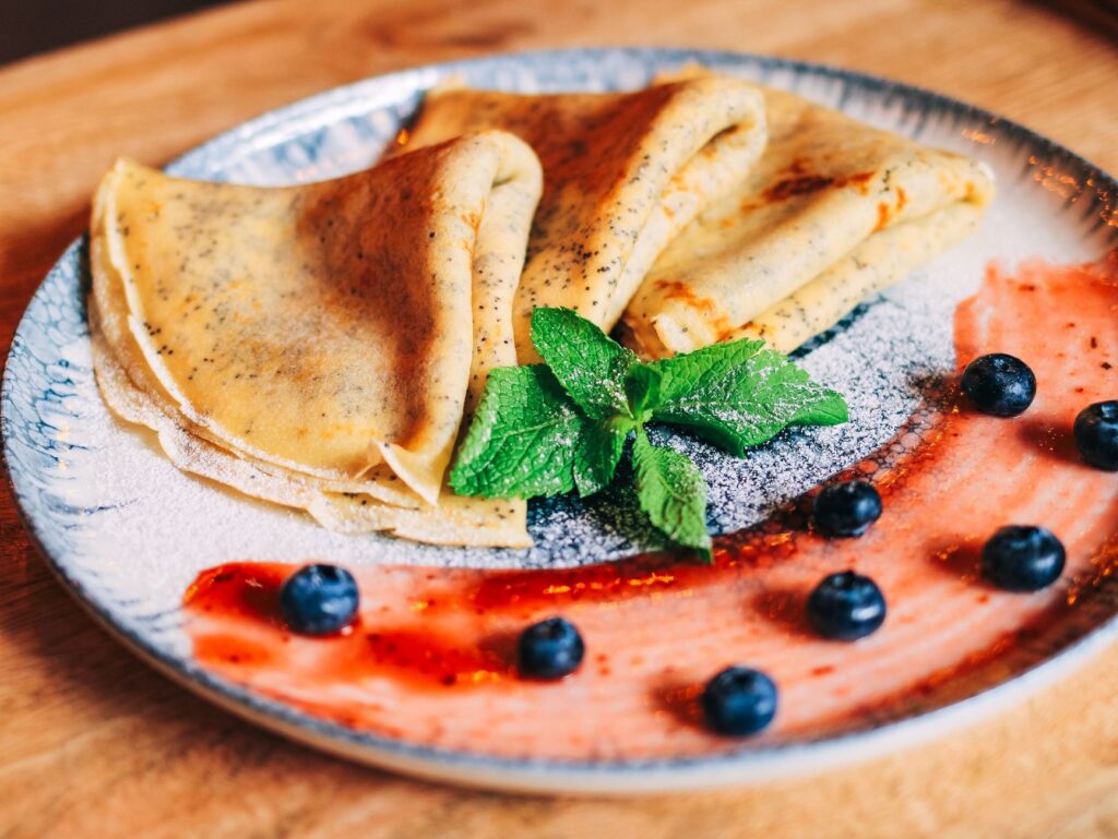 De délicieuses crêpes garnies de sauce aux myrtilles, à la menthe et aux fraises, présentées sur une assiette décorative.