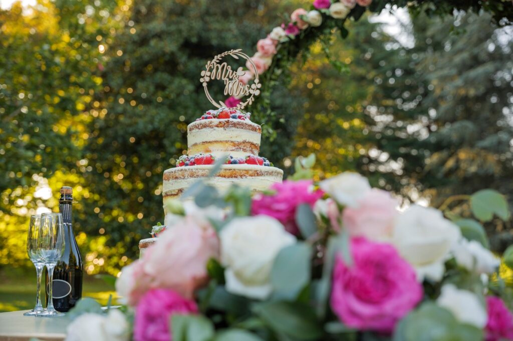 Gâteau de mariage nu avec décor floral dans un cadre de jardin, parfait pour une célébration estivale.