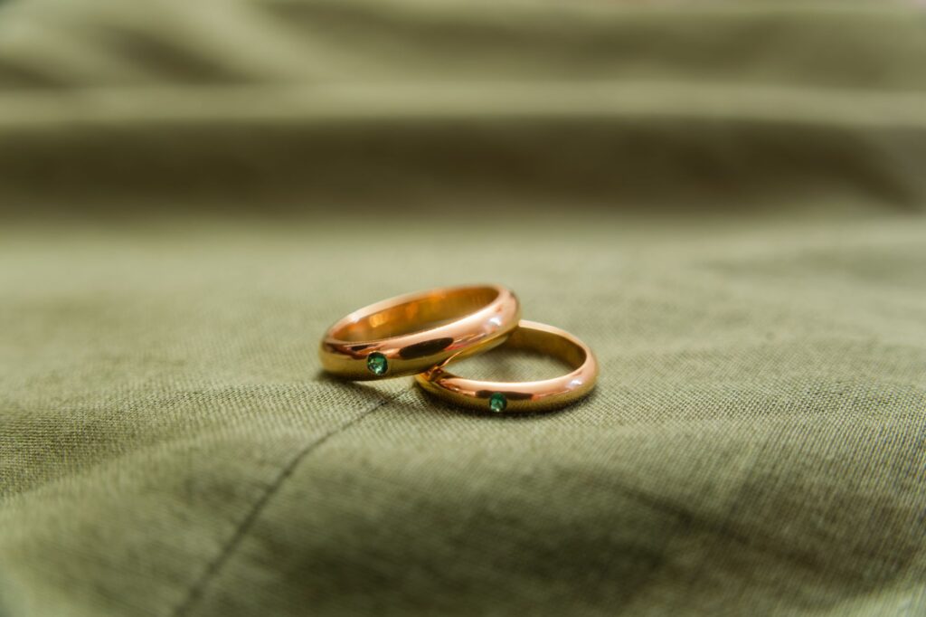 Gros plan sur deux bagues de mariage en or sur un tissu, accentuées de pierres précieuses émeraude, symbolisant l'engagement et l'amour.