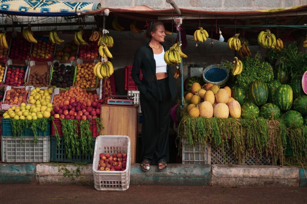 Une femme se tient près d'un étal de fruits colorés à Oued Ed-Dahab, proposant des bananes, des melons et bien d'autres choses encore.