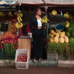 Une femme se tient près d'un étal de fruits colorés à Oued Ed-Dahab, proposant des bananes, des melons et bien d'autres choses encore.