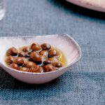 Gros plan sur des olives fraîches disposées dans un plat sur un tissu bleu texturé, évoquant la cuisine méditerranéenne.