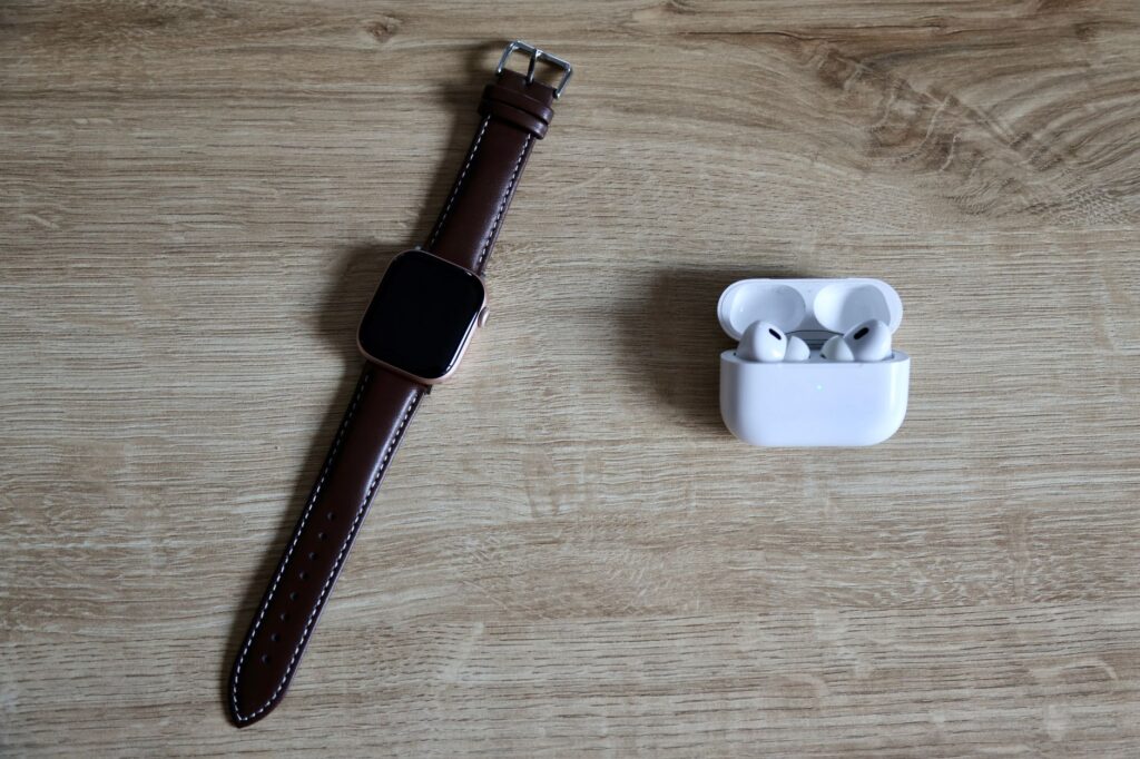Vue à plat d'une montre connectée et d'écouteurs sans fil sur une surface en bois, mettant en valeur les essentiels du quotidien moderne.