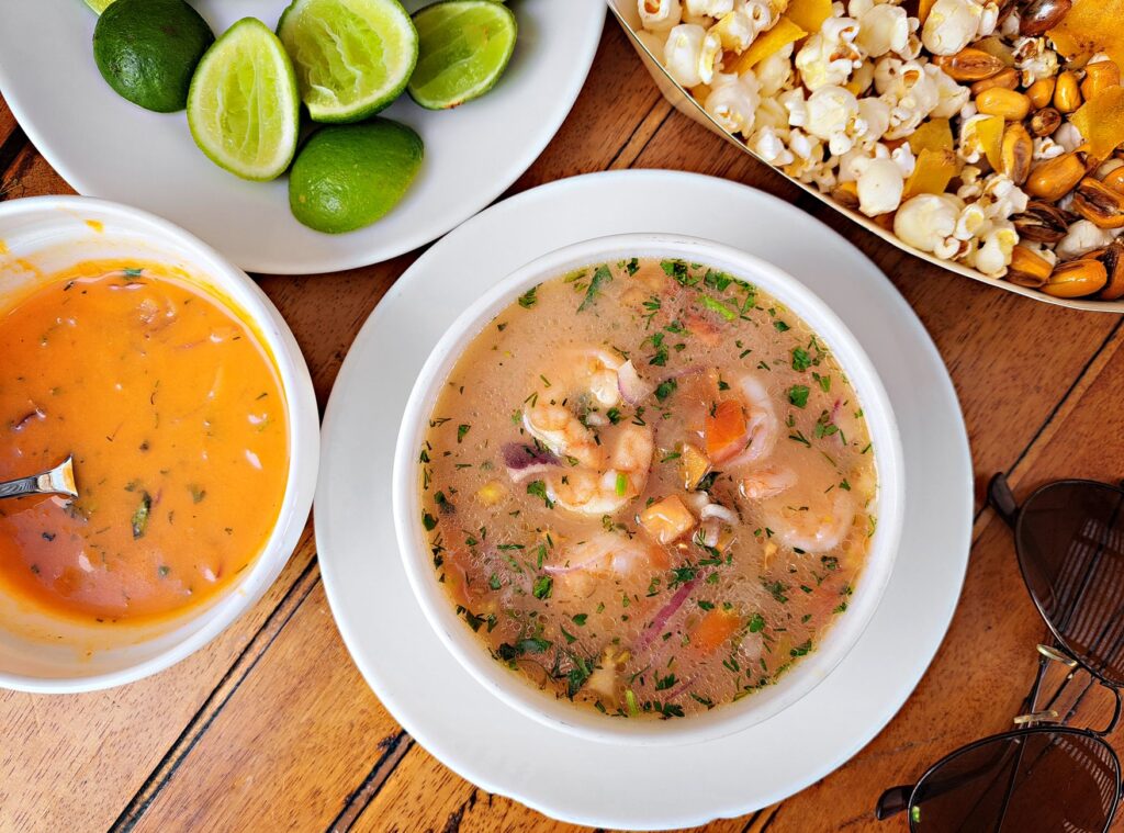 Un bol coloré de ceviche équatorien accompagné de citrons verts, de noix et de pop-corn, servi sur une table en bois.