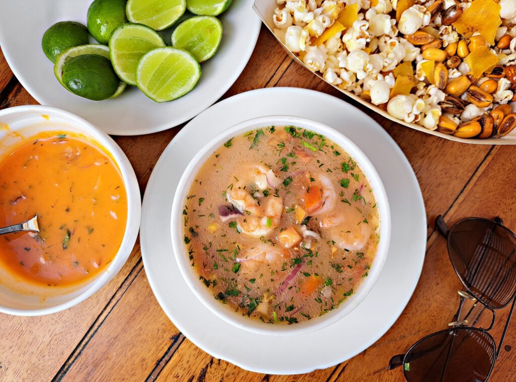 Un délicieux ceviche de fruits de mer équatorien, accompagné de citron vert, de pop-corn et de sauces, servi sur une table en bois.