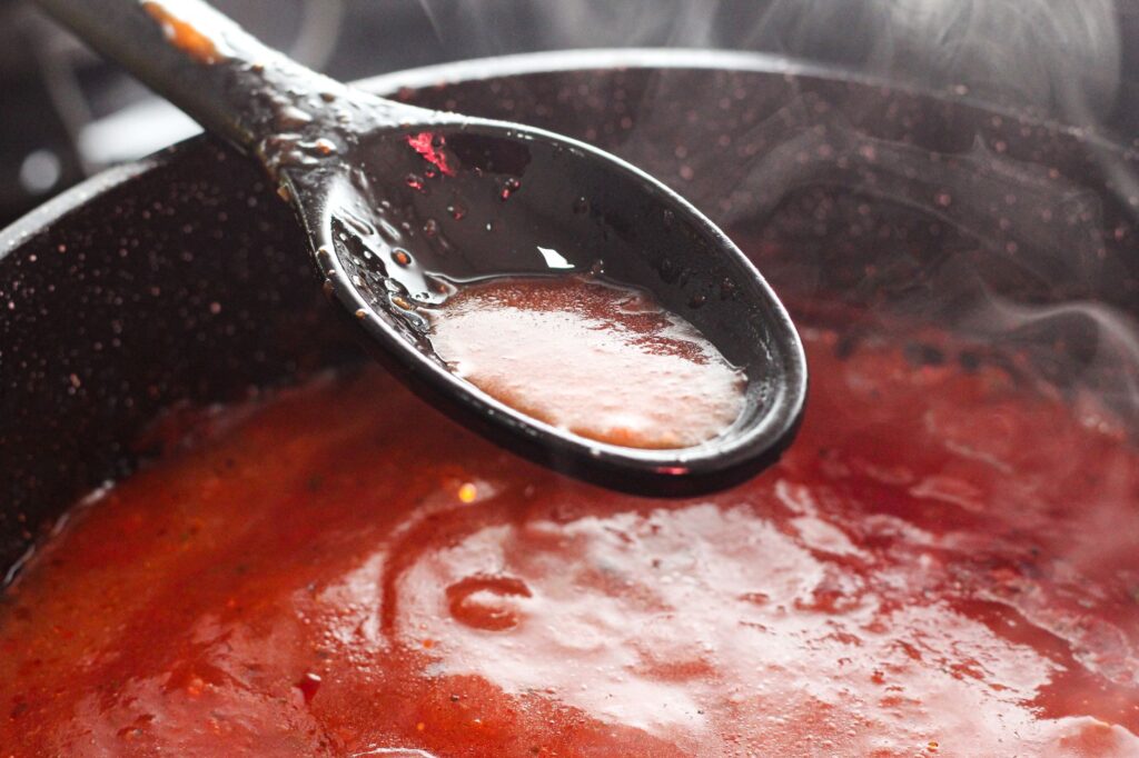 Sauce tomate fumante qui mijote dans une casserole, on en prélève une portion à l'aide d'une louche.
