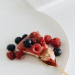 Gros plan sur une part de cheesecake avec des framboises et des myrtilles fraîches dans une assiette.