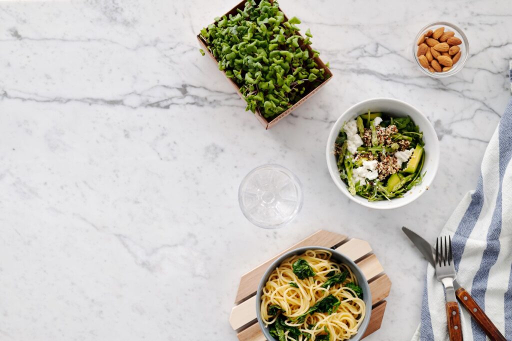 Vue de dessus d'un repas nutritif avec salade et pâtes sur une surface en marbre, parfait pour des thèmes de alimentation saine.