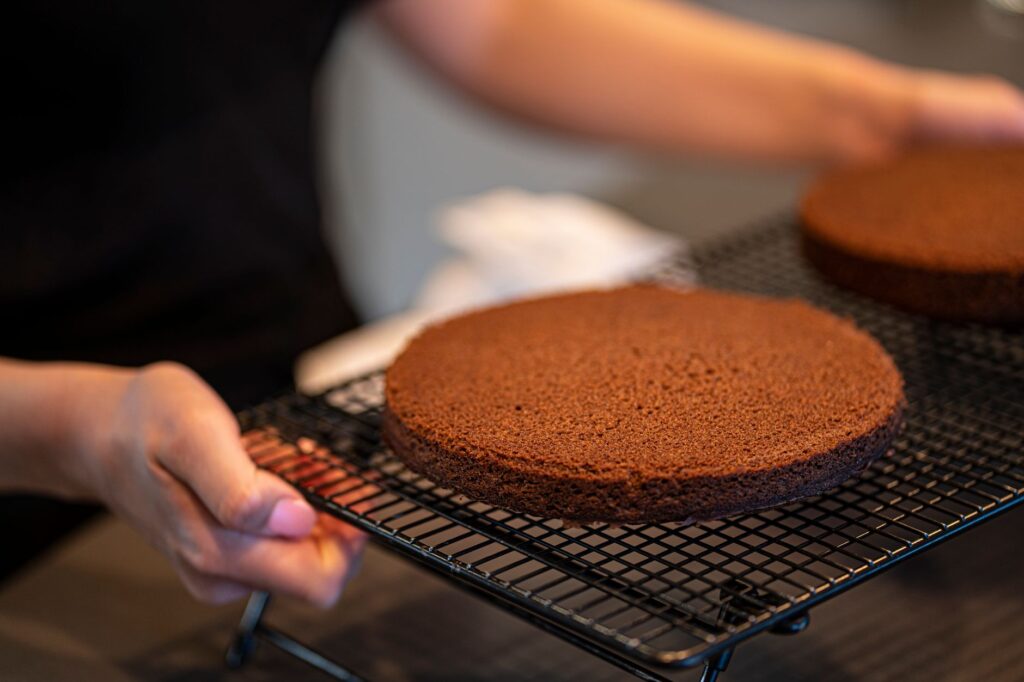 Des mains plaçant des couches de gâteau au chocolat fraîchement cuites sur une grille de refroidissement dans une cuisine familiale.