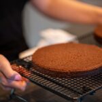 Des mains plaçant des couches de gâteau au chocolat fraîchement cuites sur une grille de refroidissement dans une cuisine familiale.