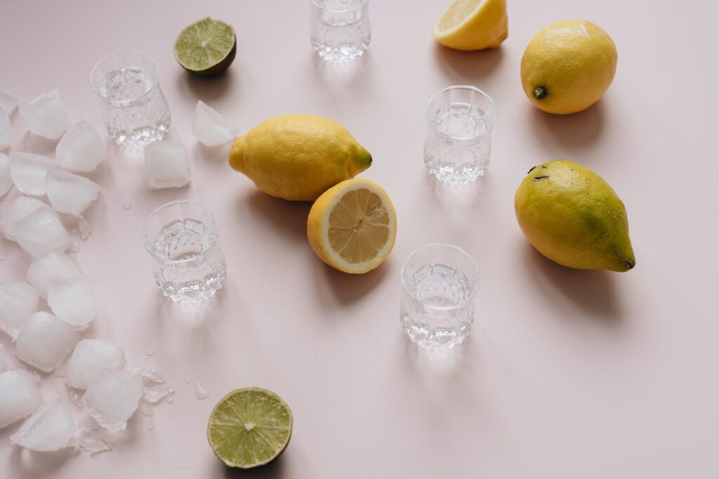 Vue du dessus de citrons, limes, glaçons et verres à shot sur une surface claire.