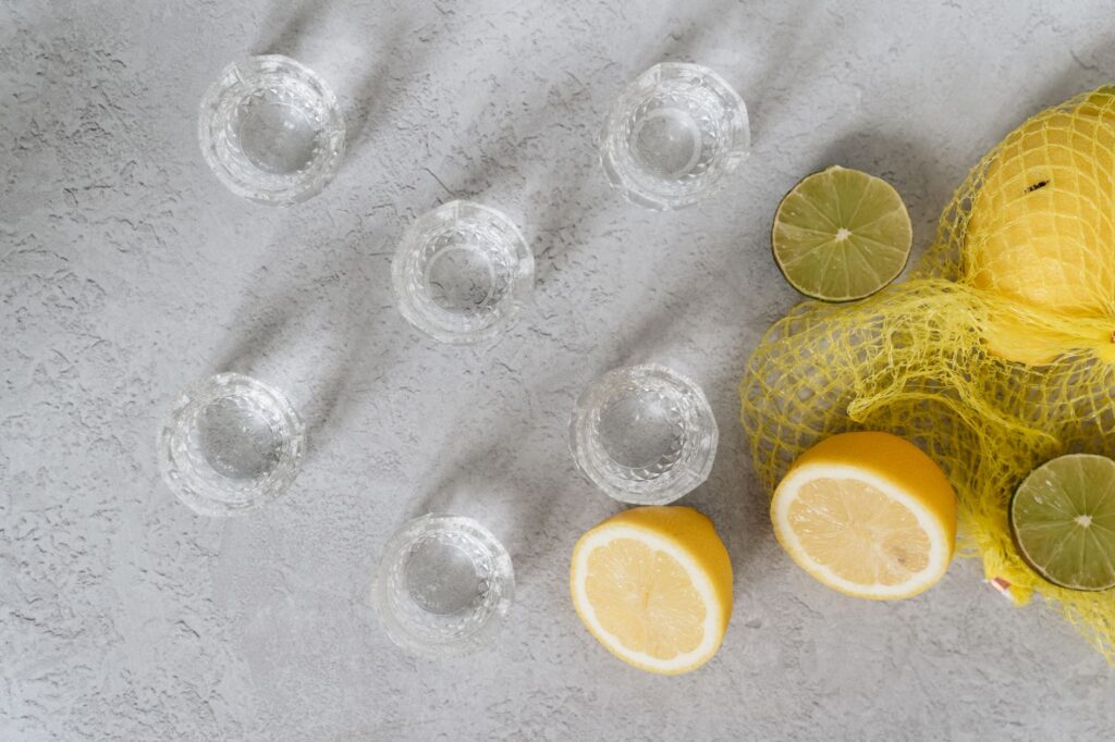 Des citrons frais et des verres à shot disposés sur une surface texturée, idéaux pour des thèmes de boissons ou culinaires.