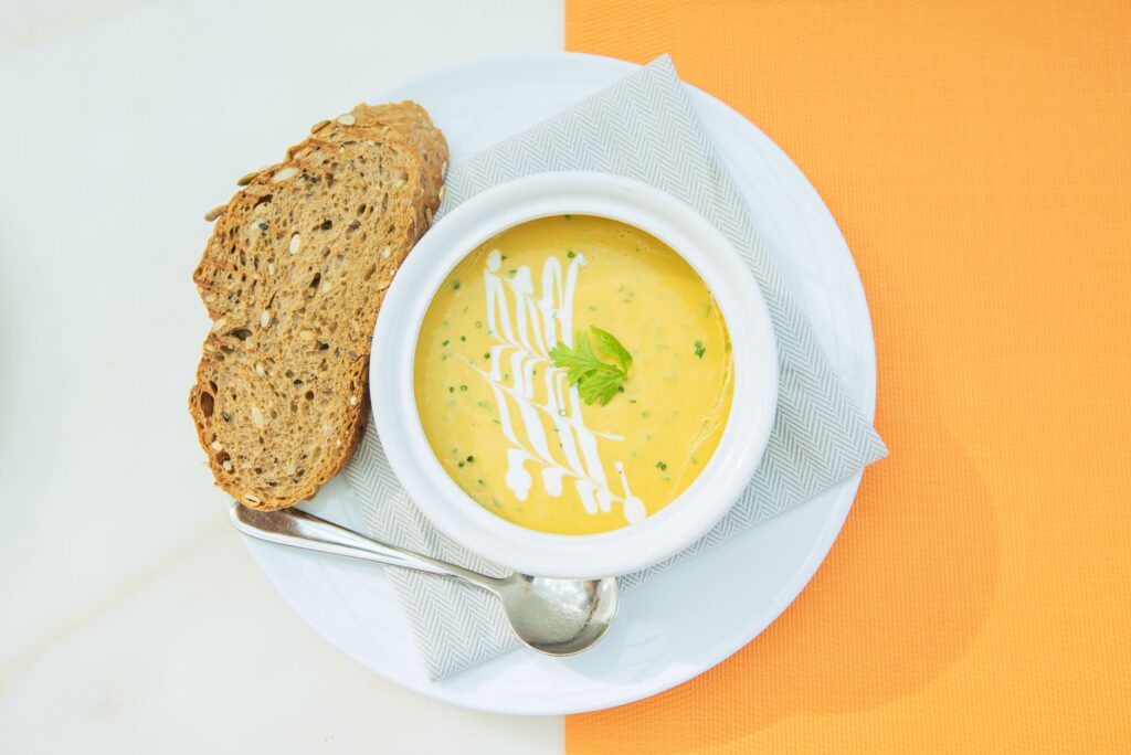 Un bol de soupe de légumes crémeuse garnie de crème et d'herbes, servie avec du pain artisanal.