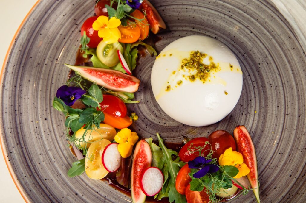 Un plat vibrant avec des légumes frais et du fromage burrata crémeux sur une assiette décorative.