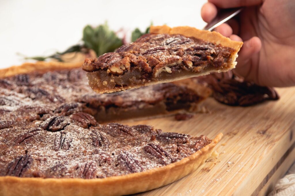 Gros plan sur une main tenant une part de tarte aux pacanes faite maison avec une pincée de sucre glace.