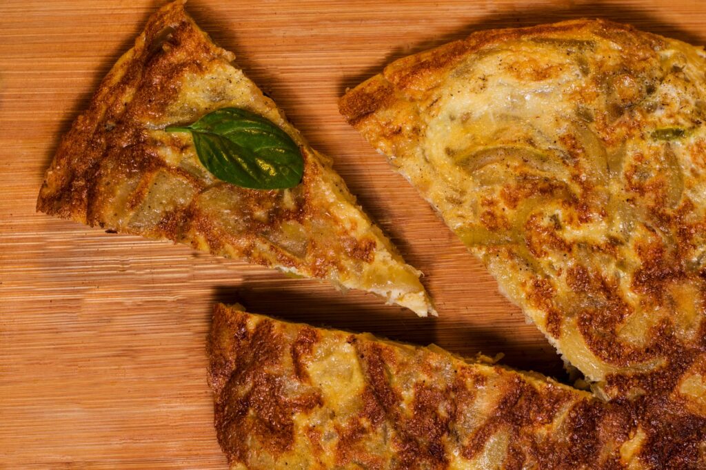Gros plan de tranches de tortilla espagnole traditionnelles sur une planche en bois, garnies de basilic.