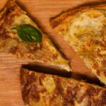 Gros plan de tranches de tortilla espagnole traditionnelles sur une planche en bois, garnies de basilic.