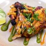 Délicieux poulet grillé épicé garni de coriandre et de citron vert, parfait pour un repas savoureux.