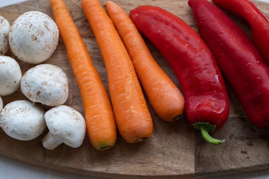 Gros plan de légumes biologiques frais, y compris des carottes, des champignons et des poivrons rouges sur une planche à découper en bois.