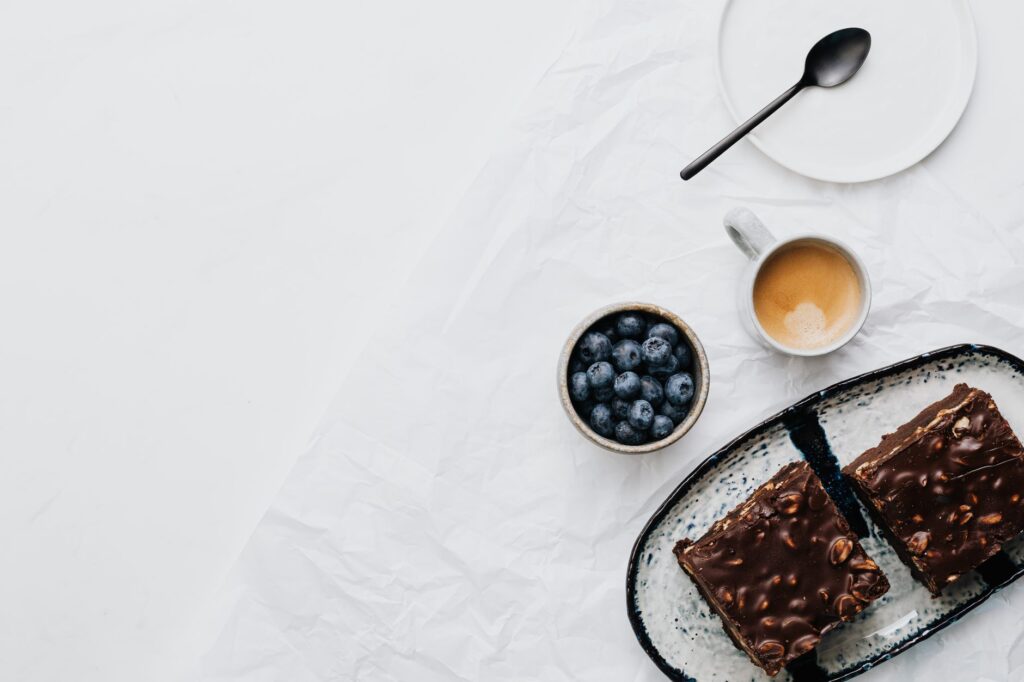 Vue en plongée d'un gâteau au chocolat, de myrtilles et d'un café sur un fond blanc.