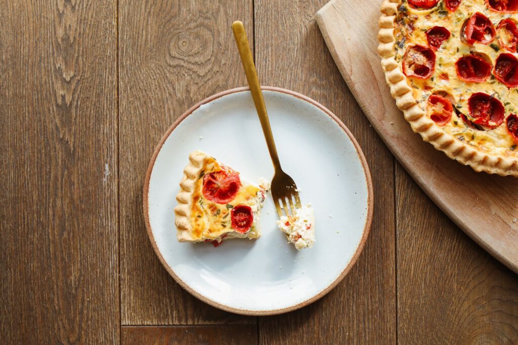 Gros plan sur une délicieuse part de quiche à la tomate sur une table en bois rustique.