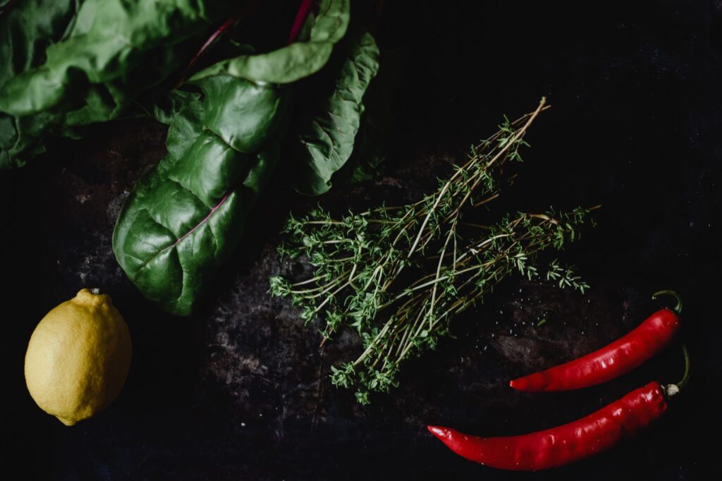Vue de dessus de bette à carde, piments, thym et citron sur fond sombre.