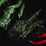 Vue de dessus de bette à carde, piments, thym et citron sur fond sombre.