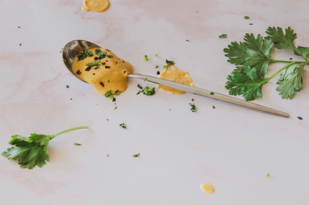 Cuillère de sauce crémeuse aux herbes avec de la coriandre fraîche sur un fond blanc.