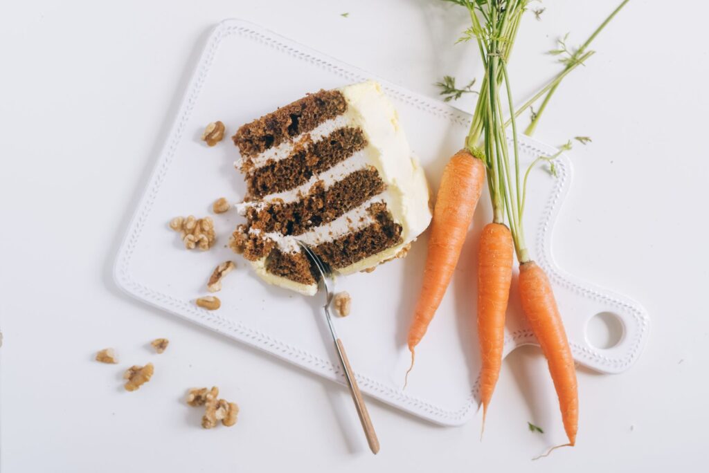 Une tranche de gâteau aux carottes gourmande avec glaçage, noix et carottes fraîches sur une planche à découper.