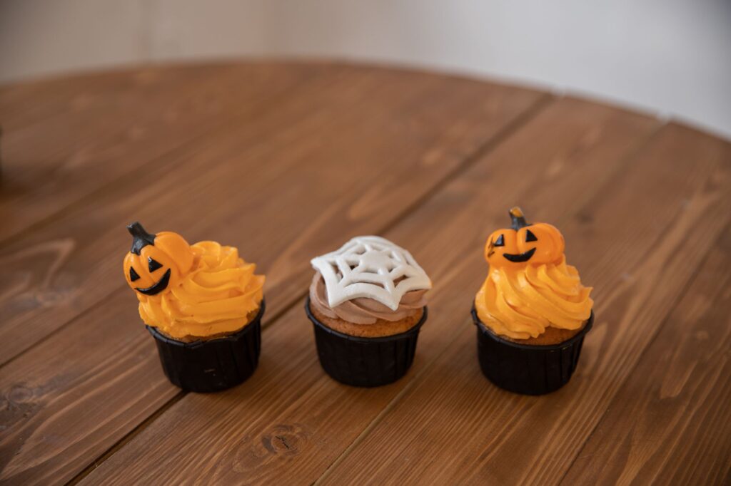 Trois cupcakes sur le thème d'Halloween avec des motifs de citrouille et de toile d'araignée sur une table en bois.