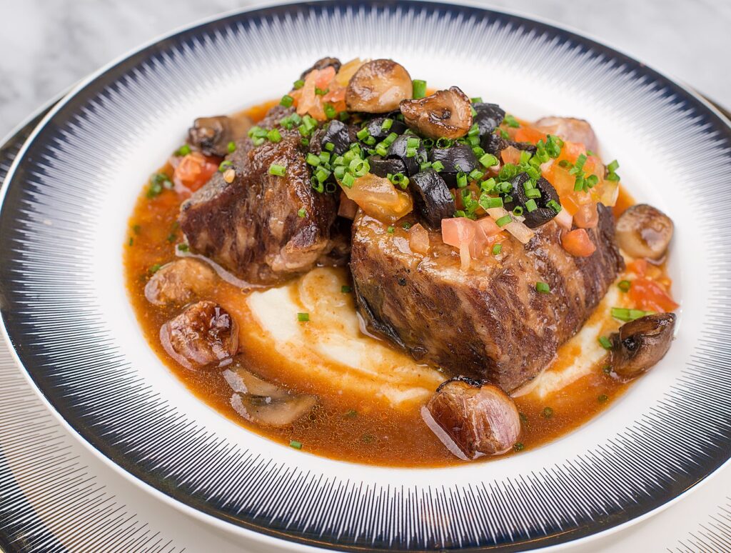 Côtes de bœuf braisées avec des champignons et de la ciboulette sur une purée de pommes de terre.