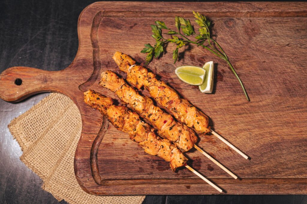Brochettes de poulet grillé juteuses sur une planche en bois avec du citron vert et des herbes.